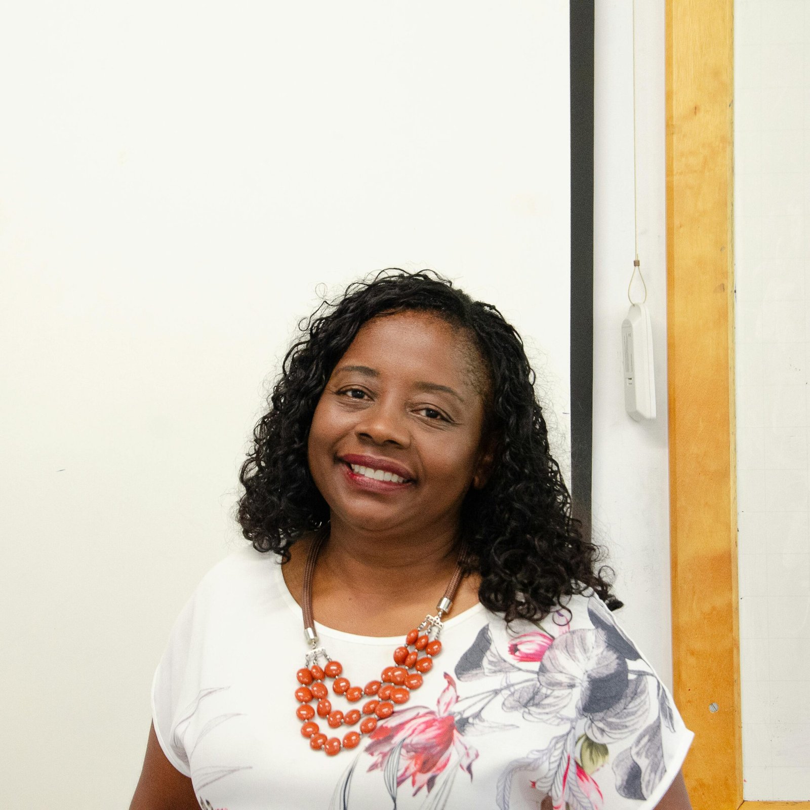 Charming portrait of a smiling woman with curly hair in a floral blouse and orange necklace.